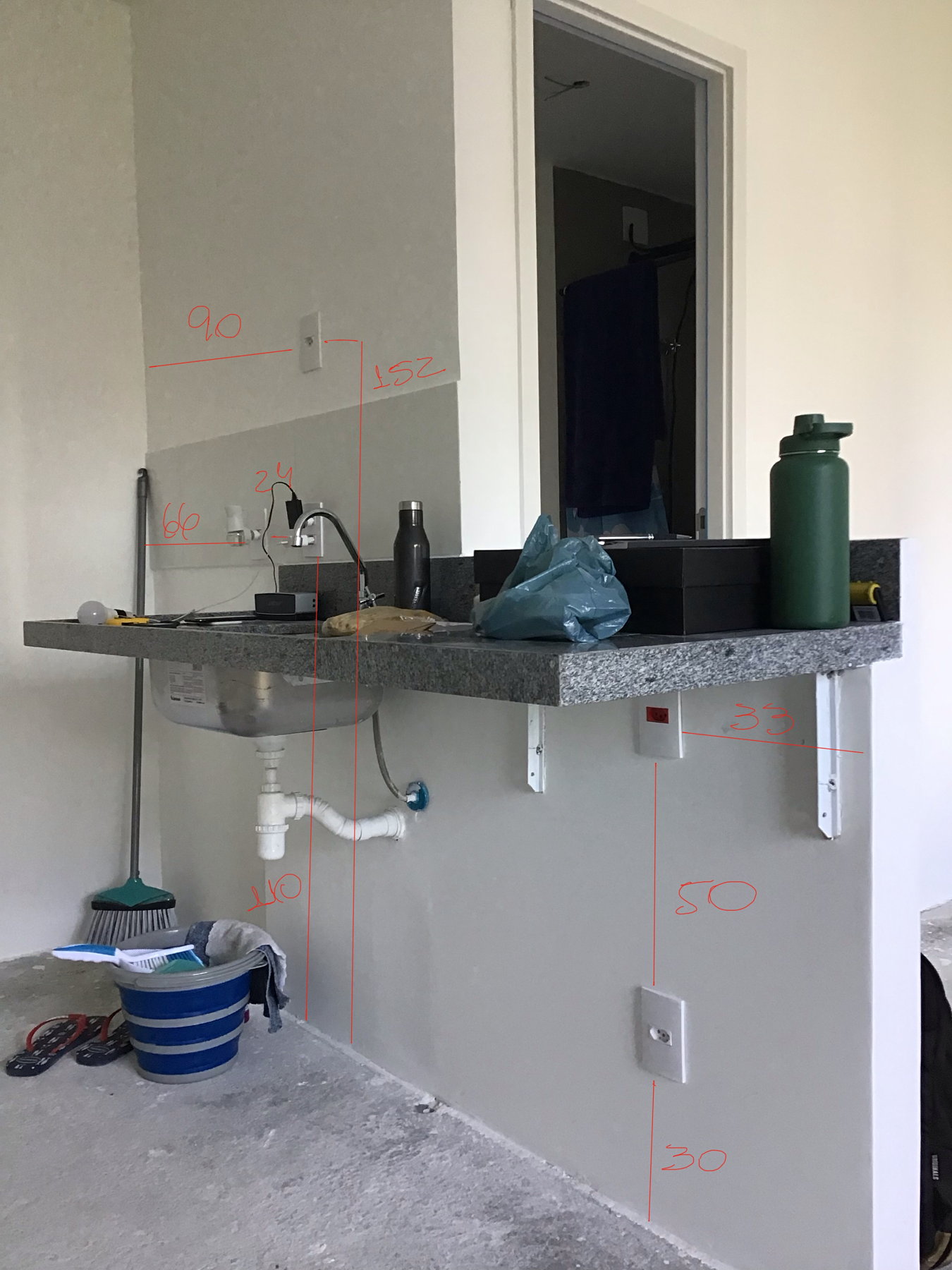 Bancada de cozinha da construtora com as medidas escritas em vermelho sobre a parede: altura da bancada e posição dos pontos de água e das tomadas
