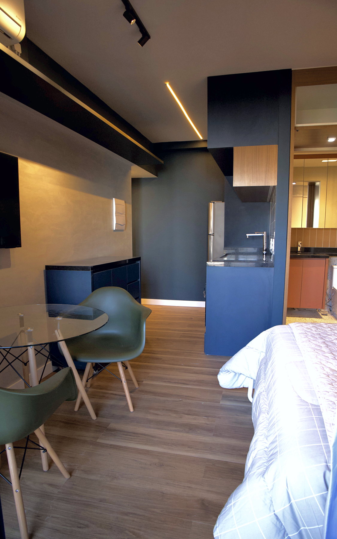 Vista geral do studio pronto, da mesa de jantar até a cozinha e a porta aberta do banheiro, com a cama escamoteável aberta à direita