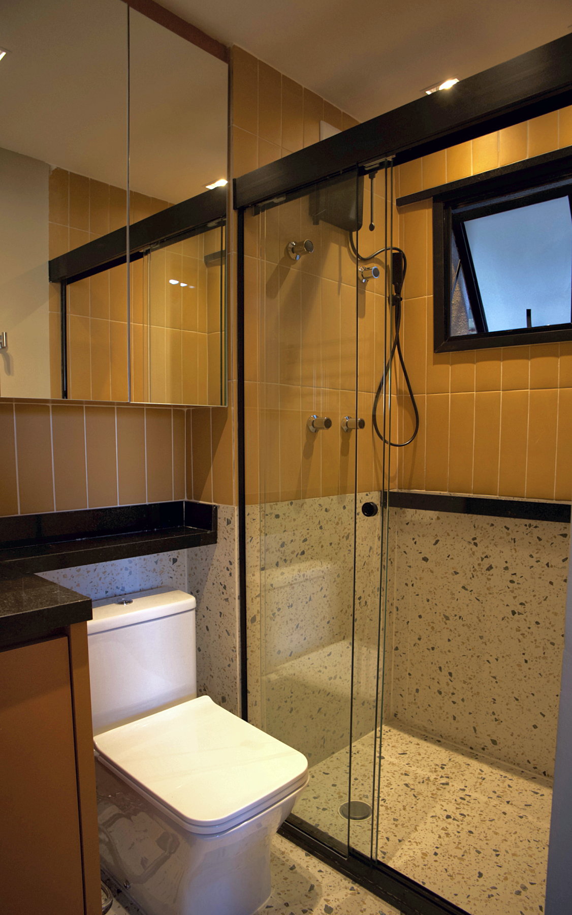 Box do banheiro com três folhas de vidro, revestimento vertical terracota Terralma, meia-parede em porcelanato Confete e janela