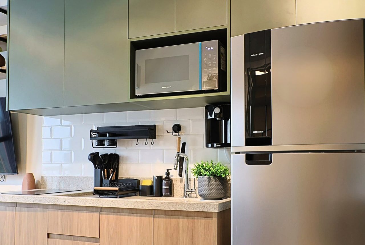 Cozinha compacta com marcenaria verde, geladeira inox, micro-ondas e azulejo branco