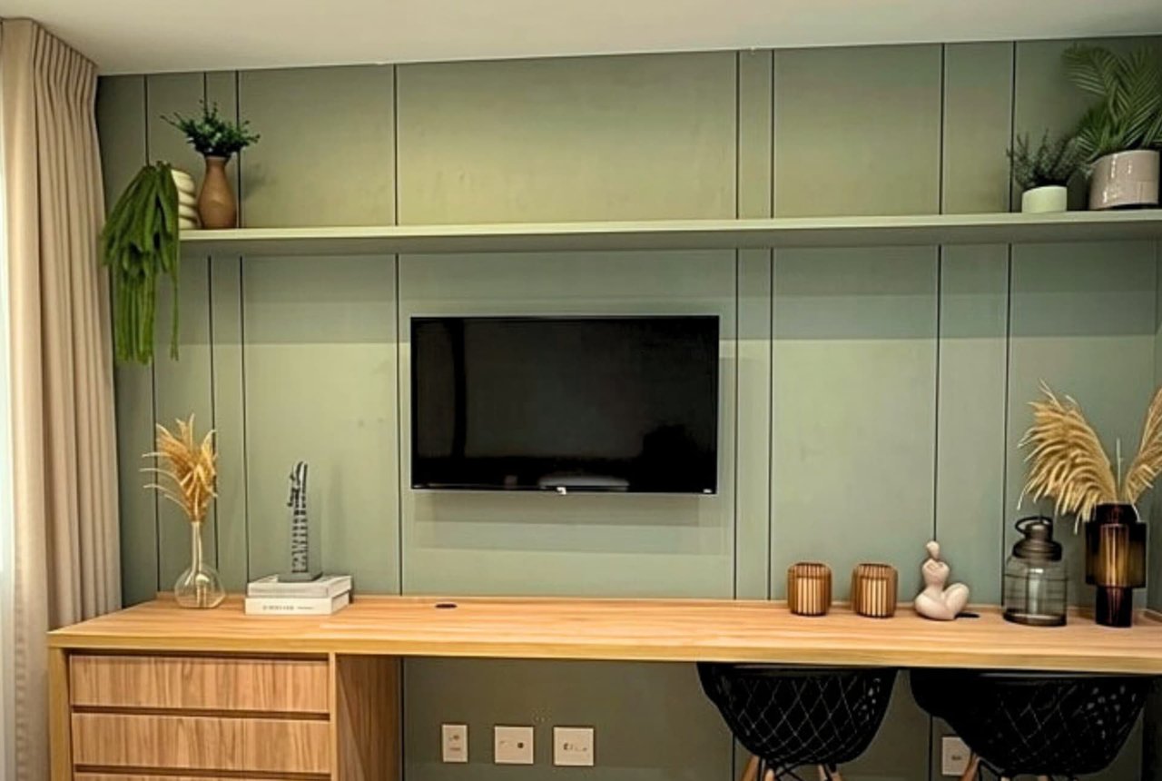 Marcenaria planejada com painel verde-claro, bancada de madeira, TV na parede e prateleira com plantas