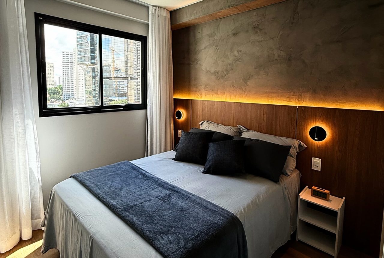 Quarto com painel de madeira iluminado por fita de LED quente, parede de cimento queimado e janela com vista da cidade