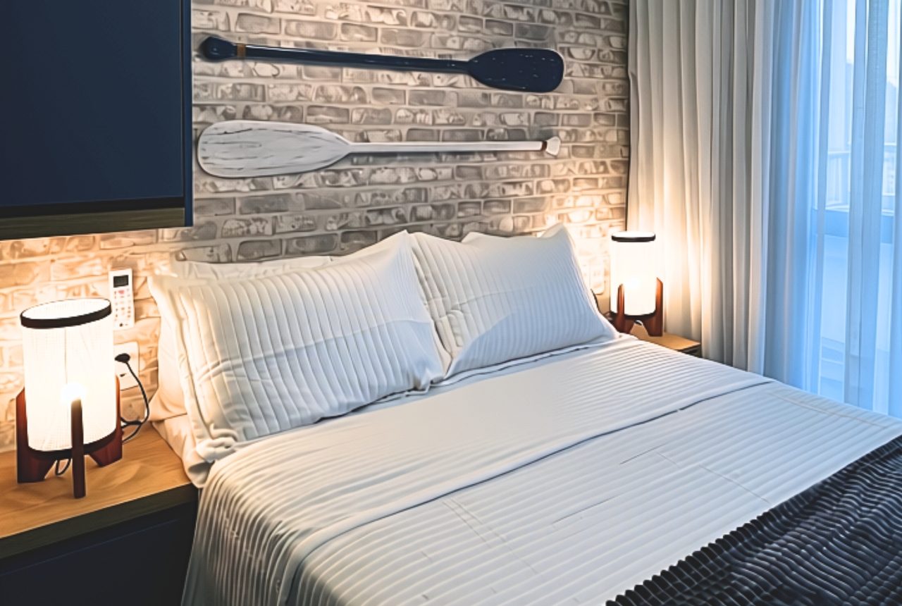Quarto com parede de tijolos claros, remos decorativos, roupa de cama branca e guarda-roupa azul-marinho