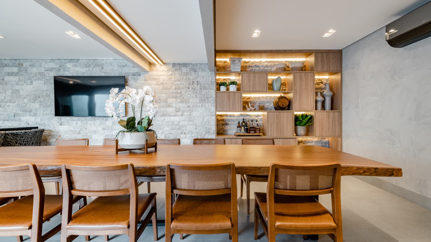 Sala de jantar integrada reformada pela Bewild para moradia, com mesa de madeira maciça, parede de pedra e marcenaria iluminada